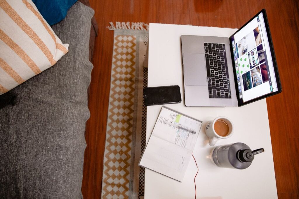 Visão aérea de mesa de centro com laptop, celular, caderno e xícara de café, ilustrando a organização de um espaço de trabalho remoto.