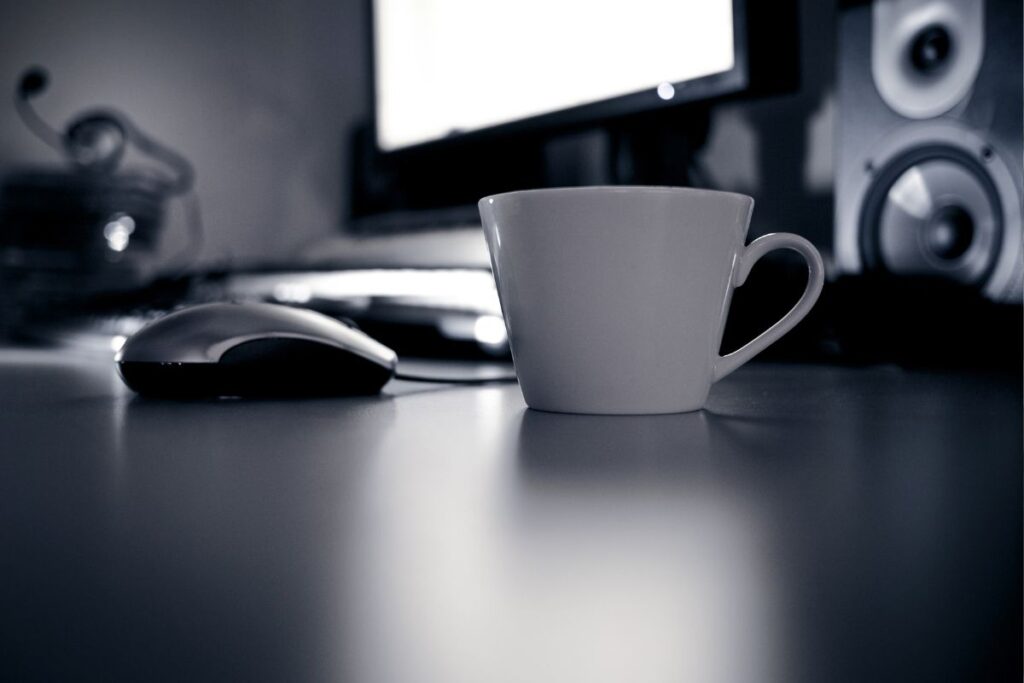 Xícara de café branca e mouse de computador em mesa, simbolizando ferramentas básicas para um dia de trabalho.