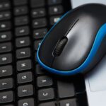 Mouse sem fio azul e preto sobre um teclado de laptop, ideal para setups compactos de home office.