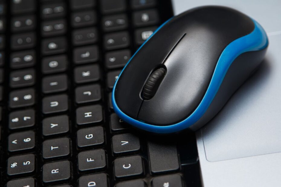 Mouse sem fio azul e preto sobre um teclado de laptop, ideal para setups compactos de home office.