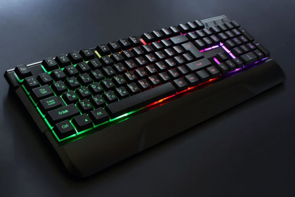 Teclado gamer com retroiluminação RGB colorida em ambiente escuro, sugerindo um teclado de alta performance para digitar e jogar.