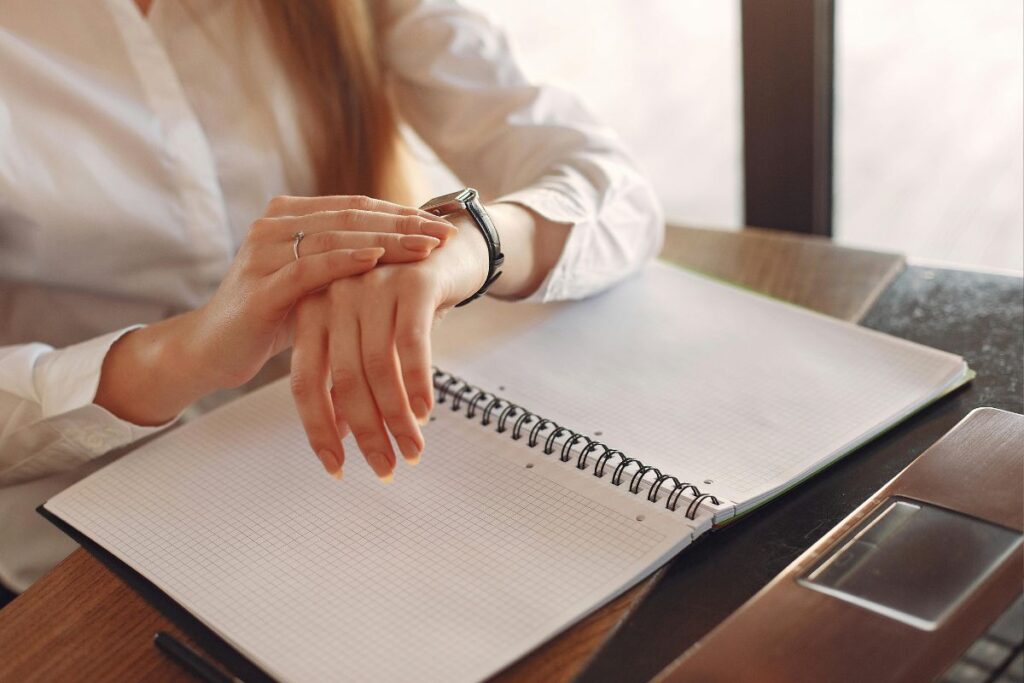 Mulher verificando o relógio no pulso com caderno aberto na mesa representando o controle de tempo na técnica pomodoro