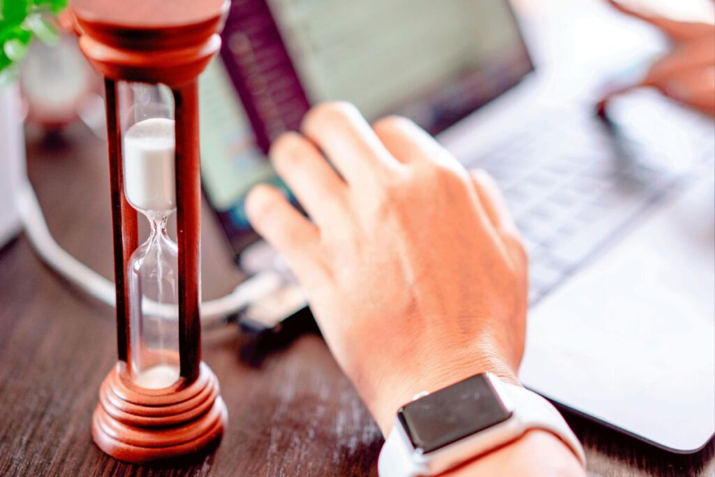 Pessoa digitando no notebook com ampulheta ao lado simbolizando os intervalos de tempo do método pomodoro de produtividade