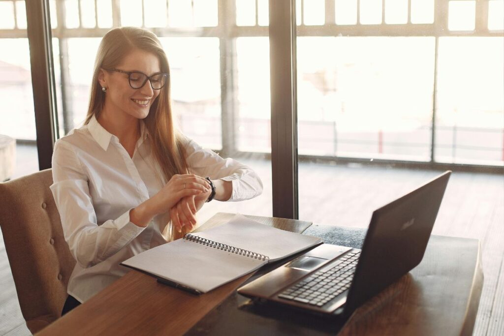 Mulher sorrindo enquanto verifica o relógio durante sessão de trabalho com a técnica de gestão do tempo