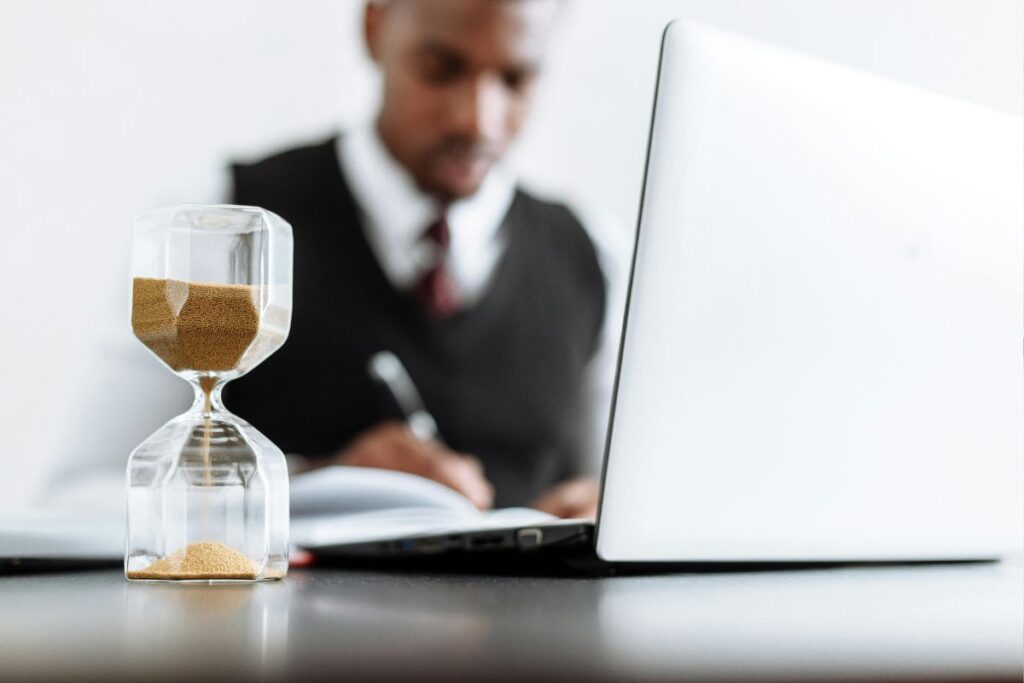 Imagem de uma mulher jovem sorrindo ao verificar o relógio de pulso em uma mesa com caderno e notebook abertos, com luz natural ao fundo — transmitindo a sensação de controle, satisfação e bem-estar que a técnica proporciona ao transformar a relação com o tempo e a produtividade no dia a dia.